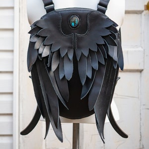 May include: Black leather backpack with large wings made of leather. The backpack has a turquoise gemstone on the front.