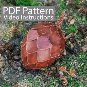 Puede incluir: Una bolsa de cuero marrón con forma de piña con una correa. La bolsa está hecha de muchos pequeños trozos de cuero cosidos juntos. El texto "PDF Pattern Video Instructions" está en la parte superior de la imagen.