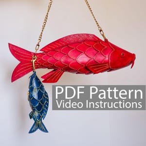 Puede incluir: Un bolso grande rojo con forma de pez y un monedero más pequeño azul con forma de pez, ambos de cuero con costuras detalladas. Cuelgan de cadenas doradas. El texto "PDF Pattern Video Instructions" es visible.