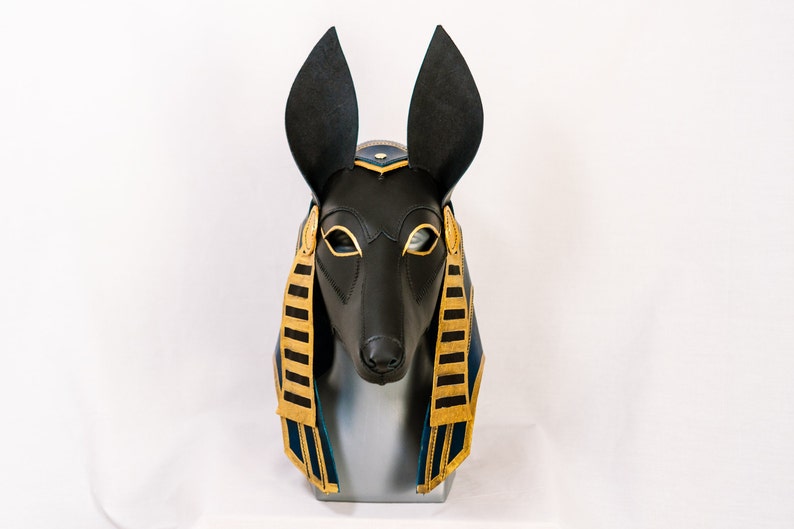 May include: A black leather Anubis mask with gold and blue accents. The mask is on a mannequin head.