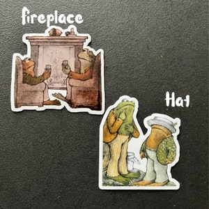 Puede incluir: Dos personajes de rana verde sentados junto a una chimenea con el texto "fireplace" encima de ellos. Otro personaje de rana verde con un sombrero y de pie con otro personaje de rana con el texto "hat" encima de ellos.