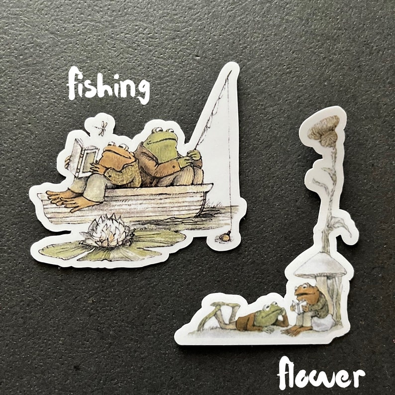 Puede incluir: Dos ranas en un bote sobre un nen&uacute;far, una est&aacute; pescando y la otra est&aacute; leyendo un libro. El texto "fishing" est&aacute; sobre el bote. Otra pegatina muestra dos ranas sentadas debajo de un hongo con el texto "flower" debajo.