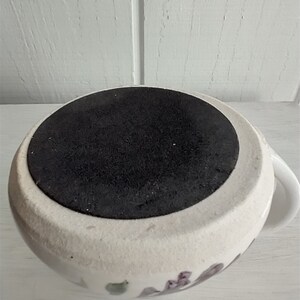 Puede incluir: Taza de cer&aacute;mica blanca con un dise&ntilde;o floral y una base de goma negra. La taza tiene un asa en el lado derecho.