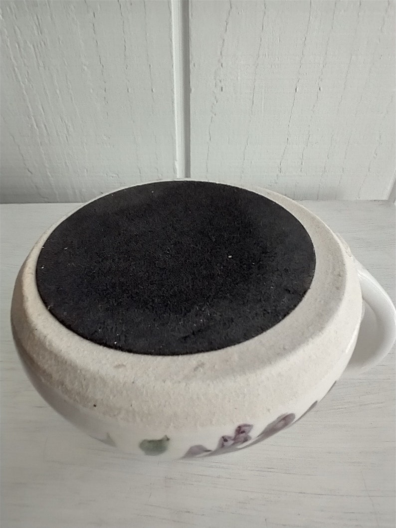 Puede incluir: Taza de cer&aacute;mica blanca con un dise&ntilde;o floral y una base de goma negra. La taza tiene un asa en el lado derecho.