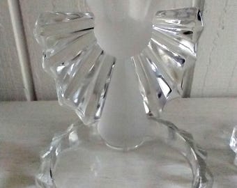 Könnte beinhalten: Ein durchsichtiger Kerzenhalter aus Glas mit einem mattierten Oberteil und einem dekorativen, gewellten Design. Der Halter hat einen runden Sockel mit einer facettierten Kante.