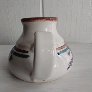 Puede incluir: Jarra de cer&aacute;mica blanca con un borde marr&oacute;n y un asa. La jarra tiene un dise&ntilde;o floral azul y verde con acentos rojos.