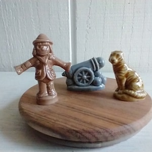 May include: Three ceramic figurines on a wooden base. A brown scarecrow figurine, a gray cannon figurine, and a brown tiger figurine.
