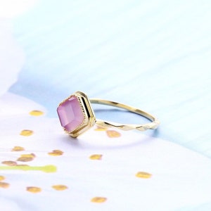 May include: A gold ring with a pink gemstone set in a geometric shape. The ring band has a textured design.