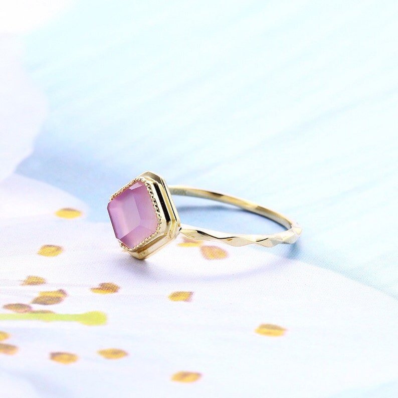 May include: A gold ring with a pink gemstone set in a geometric shape. The ring band has a textured design.