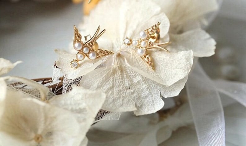 K&ouml;nnte beinhalten: Ein Paar goldene Schmetterlings-Ohrringe mit Perlen-Akzenten. Die Ohrringe sind zart und feminin und w&auml;ren ein wundersch&ouml;nes Geschenk.