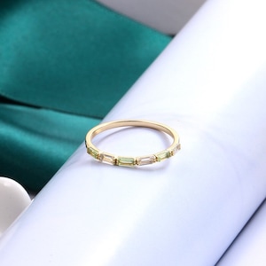 May include: A gold band ring with a row of small, rectangular green and clear gemstones.