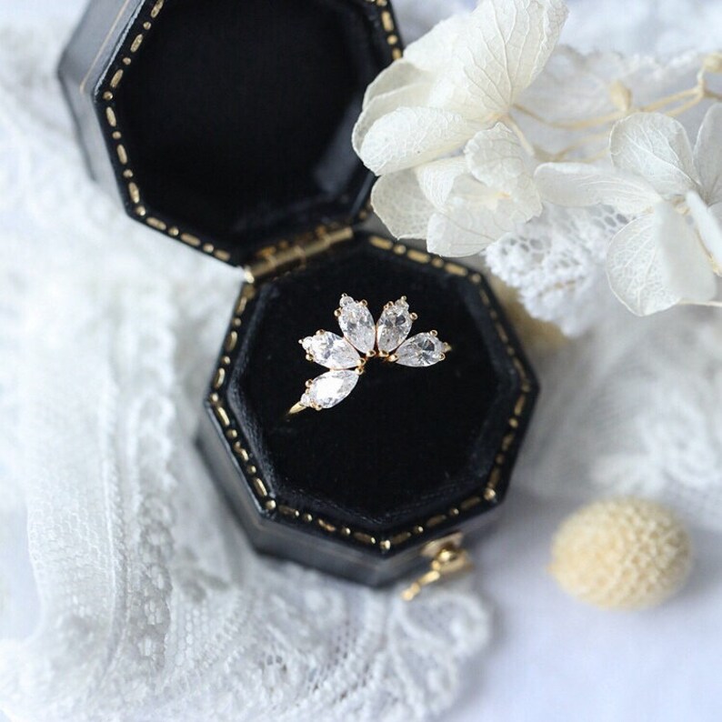 Puede incluir: Un anillo de oro con una montura de diamante en forma de marquesa. El anillo est&aacute; en una caja de anillo de terciopelo negro.