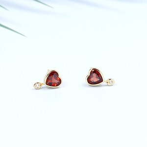 May include: A pair of gold heart-shaped earrings with a red gemstone and a small diamond accent.
