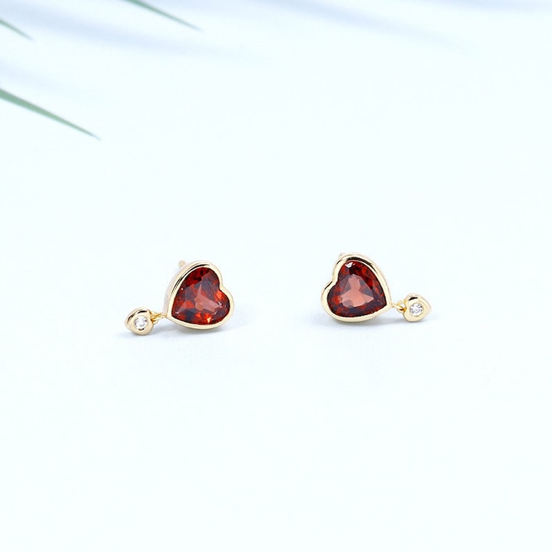 May include: A pair of gold heart-shaped earrings with a red gemstone and a small diamond accent.