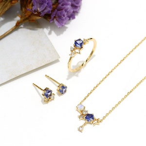May include: A gold necklace, ring and earrings set with blue and white gemstones. The necklace features a dangling blue gemstone with a star design. The ring and earrings have a similar design with a blue gemstone surrounded by smaller white gemstones.