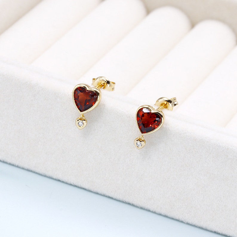 May include: A pair of gold heart-shaped earrings with red gemstone accents and a small diamond dangling from each heart.