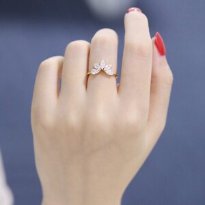 Puede incluir: Un anillo de oro con un dise&ntilde;o delicado que presenta una fila de piedras transparentes en forma de marquesa. El anillo est&aacute; puesto en un dedo con esmalte de u&ntilde;as rojo.
