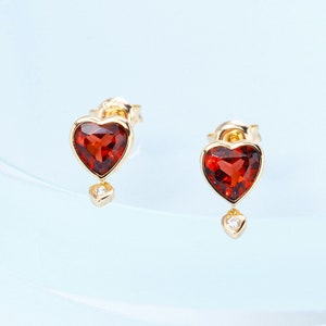 May include: A pair of gold heart-shaped earrings with red gemstones and a small diamond dangle.