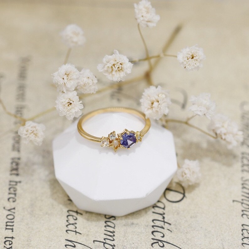 May include: A gold ring featuring a purple gemstone and small white gemstones set in a star-shaped design.