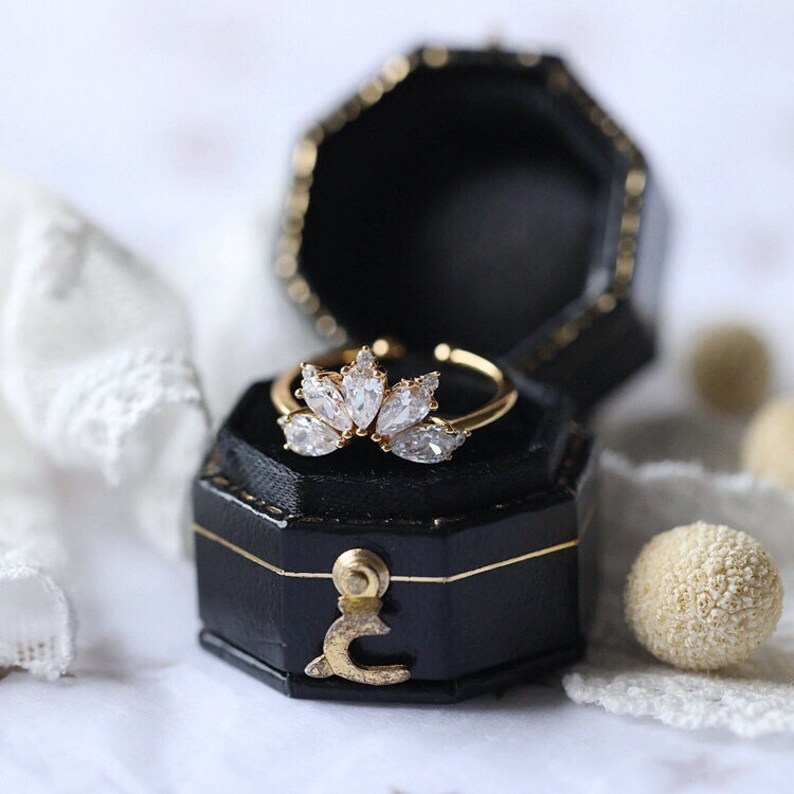Puede incluir: Un anillo de oro con un grupo de piedras transparentes en forma de pera engastadas en un dise&ntilde;o delicado y curvo. El anillo se presenta en una caja de anillo de terciopelo negro.