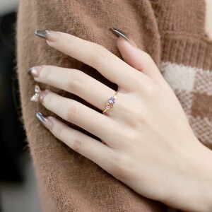 May include: A delicate gold ring featuring a small purple gemstone surrounded by smaller clear gemstones.