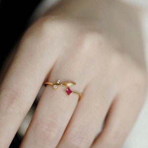 Puede incluir: Un anillo de oro con un delicado dise&ntilde;o de hoja y una peque&ntilde;a piedra preciosa roja. El anillo es abierto y ajustable.