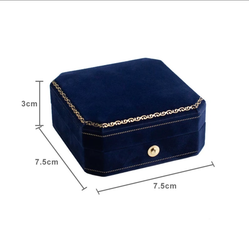 Op de afbeelding: Een blauwe fluwelen juwelendoos met een gouden rand en een klein slot. De doos meet 7,5 cm bij 7,5 cm bij 3 cm.