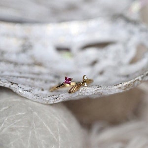 Puede incluir: Un anillo de oro con una piedra preciosa rosa y un dise&ntilde;o de hoja con una peque&ntilde;a piedra preciosa blanca.