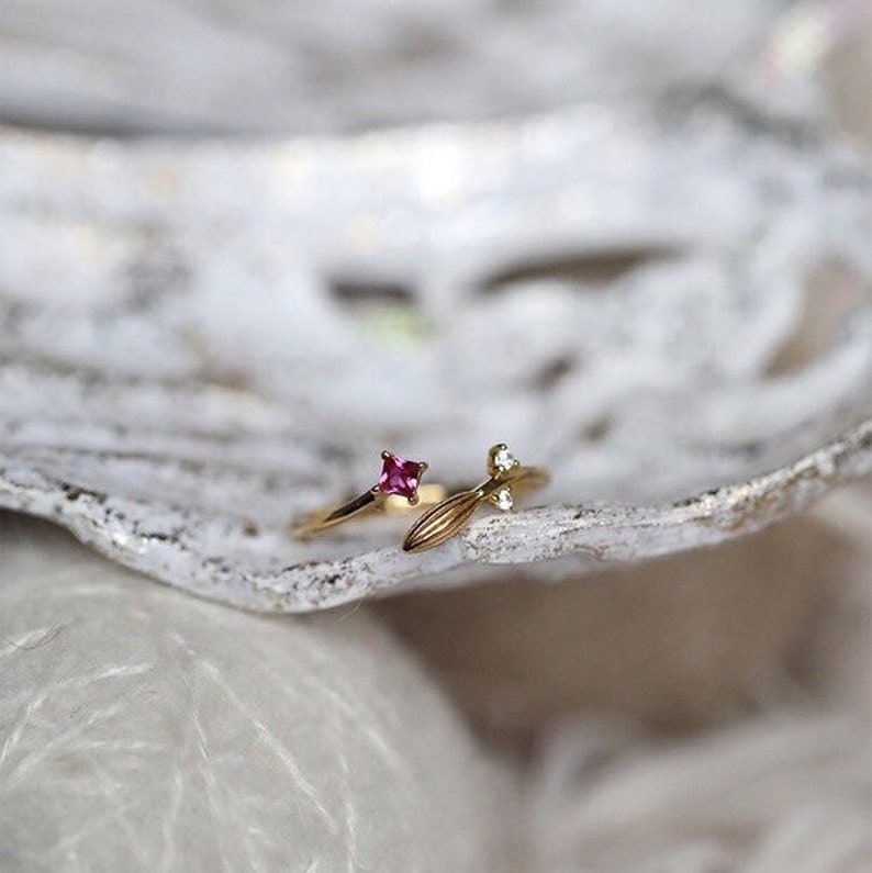 Puede incluir: Un anillo de oro con una piedra preciosa rosa y un dise&ntilde;o de hoja con una peque&ntilde;a piedra preciosa blanca.