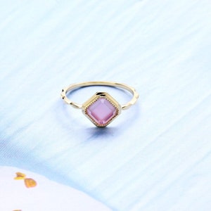 May include: A gold ring with a pink square-shaped gemstone set in a decorative frame.