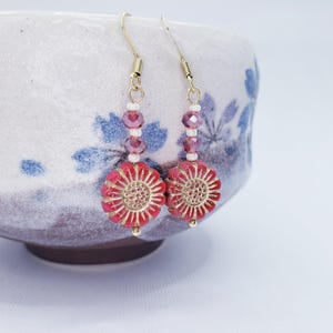 May include: A pair of dangle earrings with red and gold flower-shaped beads and clear and pink crystal beads.
