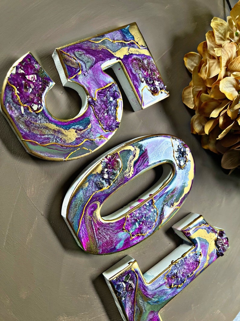 May include: Three dimensional resin numbers, 501, in a purple, gold and white colour scheme with a marbled effect and embedded glitter. The numbers are painted with a swirling, abstract design.