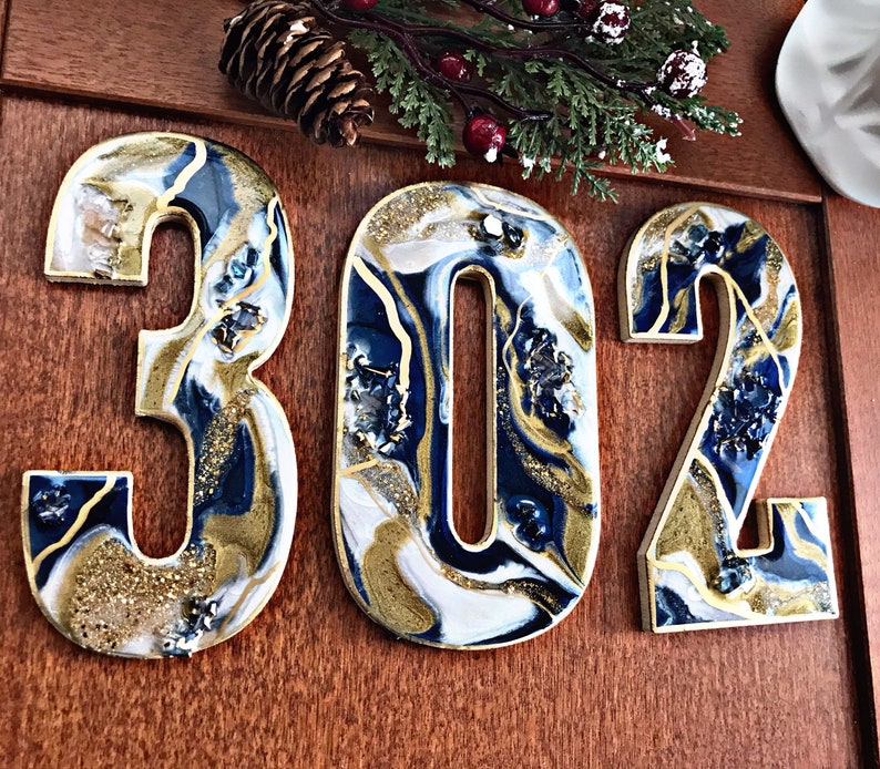 May include: Three resin house numbers, 302, in a blue, white and gold abstract design. The numbers are mounted on a wooden surface.
