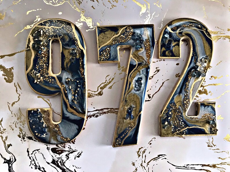 May include: Three resin numbers, 9, 7, and 2, in a blue and gold marbled design. The numbers are on a white background with gold accents.