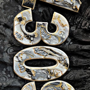 May include: White resin number ornaments with black and gold marbling and glitter accents. The numbers are 309.