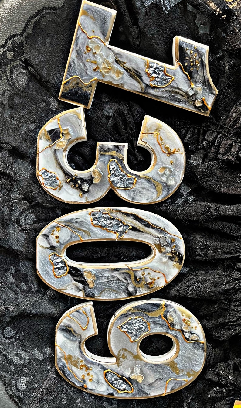 May include: White resin number ornaments with black and gold marbling and glitter accents. The numbers are 309.