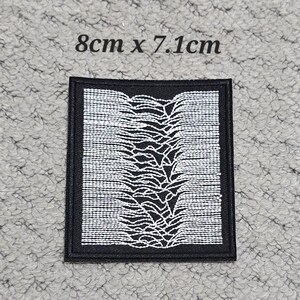 May include: Black and white embroidered patch, measuring approximately 3.15 inches by 2.8 inches. The design features a white, stylized waveform pattern on a black background, with the text "8cm x 7.1cm" above the patch.