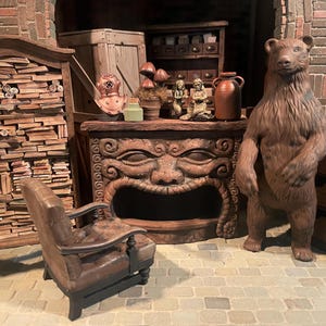 May include: A miniature dollhouse room with a brown bear figurine, a fireplace with a carved face, a bookshelf filled with books, and a small armchair.