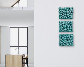 May include: Three teal blue wall sculptures made of small spheres, arranged vertically on a white wall.