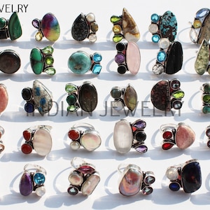 Könnte beinhalten: Eine Sammlung von 24 Silberringen mit verschiedenen Edelsteinbesatzungen. Die Ringe zeigen eine Vielzahl von Farben, darunter Rot, Blau, Grün, Lila und Pink. Die Edelsteine sind in verschiedenen Stilen gefasst, darunter Cluster, einzelne Steine und mehrsteinige Designs. Die Ringe sind alle aus Silber gefertigt und haben eine polierte Oberfläche.