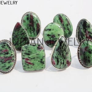 Può includere: Nove anelli d'argento con pietre preziose verdi e rosse. Gli anelli sono disposti in un gruppo su uno sfondo bianco.