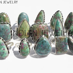 Può includere: Una collezione di 12 anelli d'argento con pietre preziose verdi e rosa. Gli anelli sono disposti in un gruppo su una superficie bianca. Le pietre preziose sono tutte di forme e dimensioni diverse.