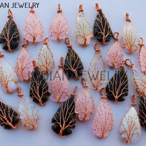 May include: A collection of 18 arrowhead-shaped pendants with copper wire tree designs. The pendants are made of black, pink, and iridescent opal-like stones.