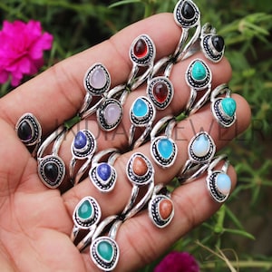 Può includere: Una collezione di anelli d'argento con accenti di pietre preziose colorate. Ogni anello presenta un design a doppia fascia con una pietra preziosa a forma di goccia incastonata in una cornice decorativa.