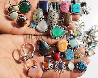 May include: A collection of silver rings with various gemstone inlays. The rings feature a variety of colors and shapes, including green, blue, red, and brown. The rings are displayed on a person's hands.