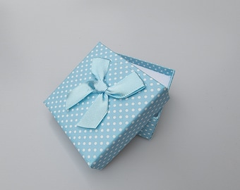May include: A light blue square gift box with white polka dots and a matching ribbon bow. The box is open, revealing a white interior. The box is likely for jewelry or small gifts.