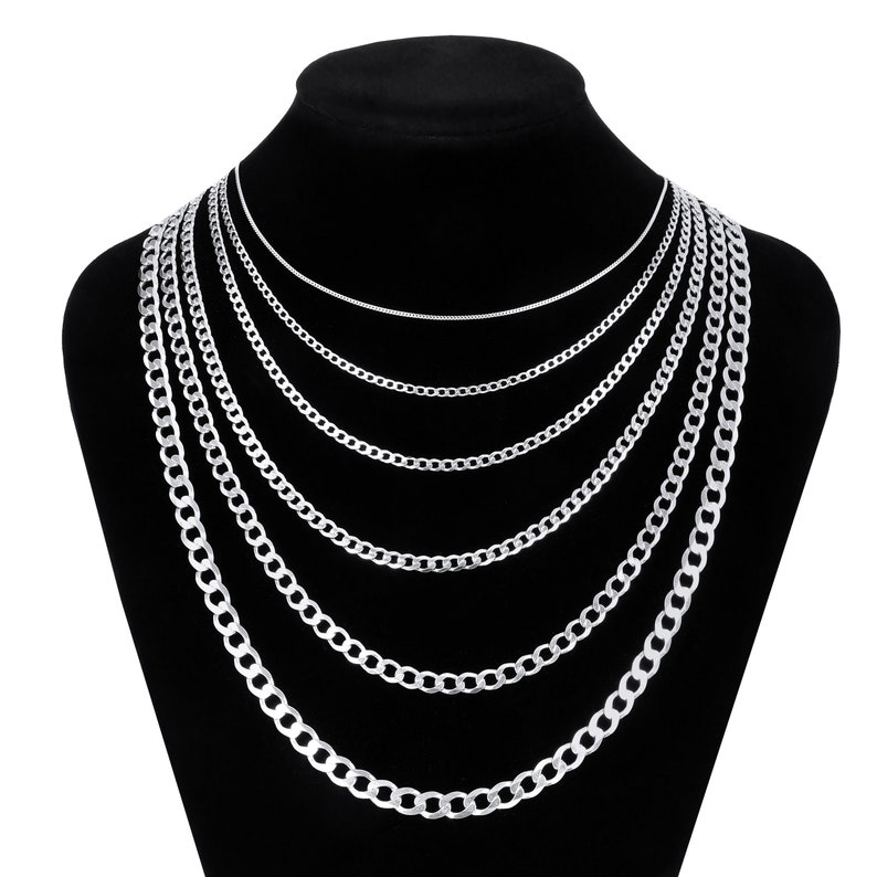 May include: A set of six silver chain necklaces of varying widths, displayed on a black velvet stand. The chains are all made of a classic curb link style.