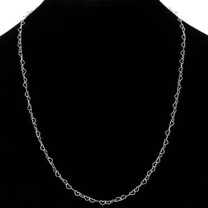May include: A delicate silver necklace featuring a repeating heart design. The necklace is displayed against a black background, highlighting the intricate details of the heart-shaped links. The chain is lightweight and appears to be made of a shiny metal.