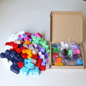 May include: A box filled with small colourful cubes, some are in a pile in front of the box. The cubes are in various colours, including red, blue, green, yellow, orange, purple, pink, and white.
