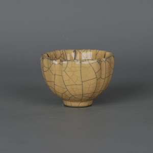 Może przedstawiać: Mała, żółta ceramiczna miska z pękniętą glazurą. Miska ma zaokrąglony kształt i lekko rozszerzający się brzeg.